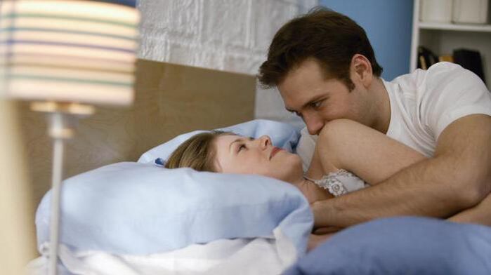 sieviete gultā ar vīrieti, kuram ir palielināts dzimumloceklis